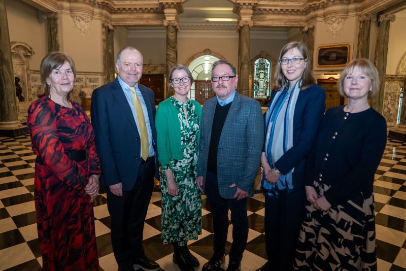 four-women-and-two-men-in-smart-dress-standing-in-a-row-on-chequered-floor